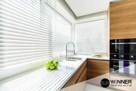 Modern bright kitchen interior with white horizontal window blinds, wooden cabinets with white countertop and household appliances
